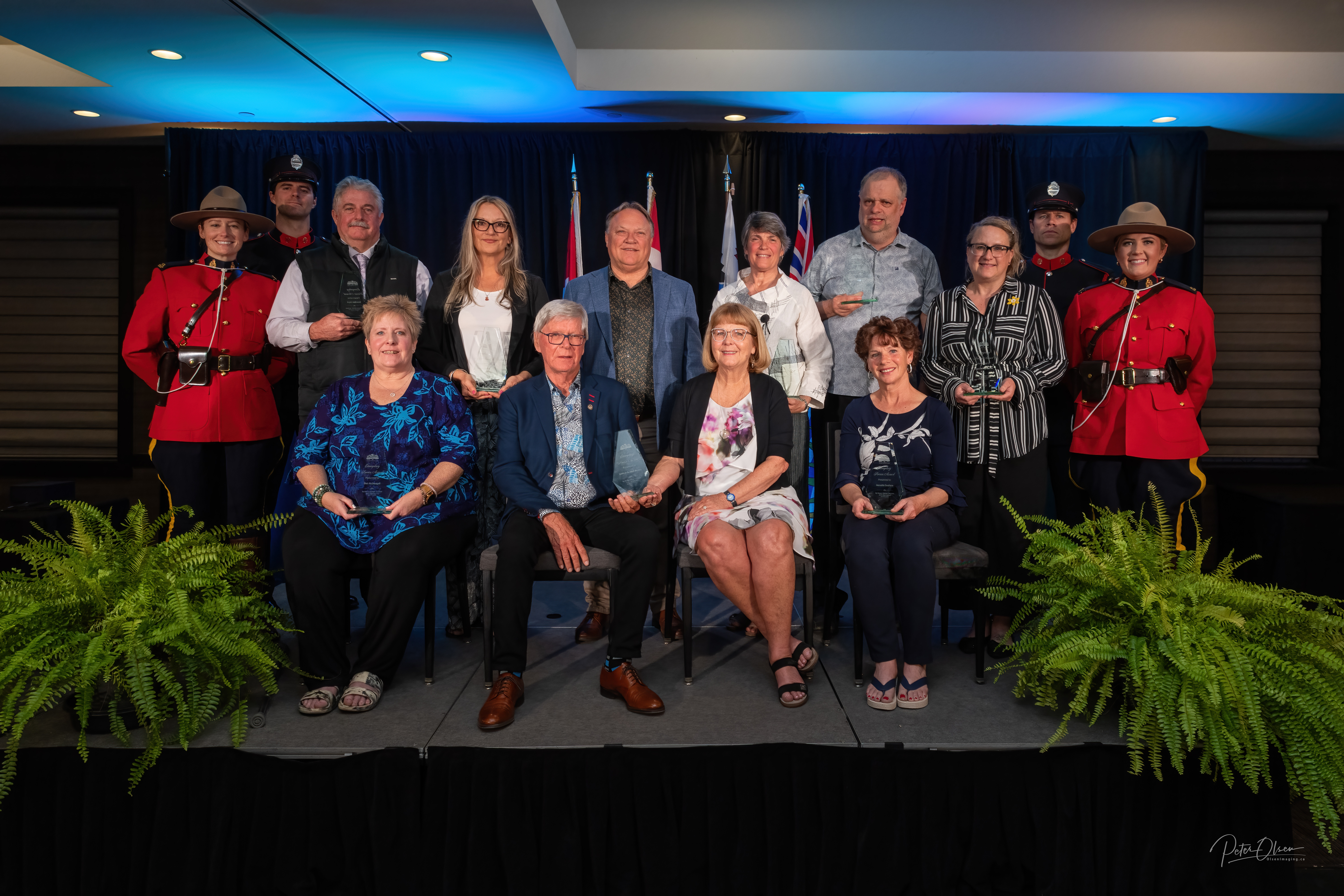 The 2024 Exemplary Service Award winners in a formal group shot each holding their awards accompanied by the Mayor and representatives from the RCMP and Fire Guard 