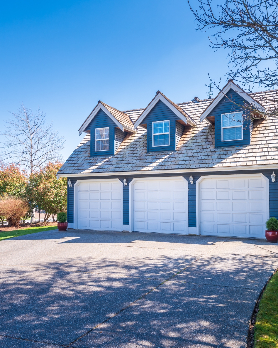 A large blue accessory building with three gables above three white garage doors.