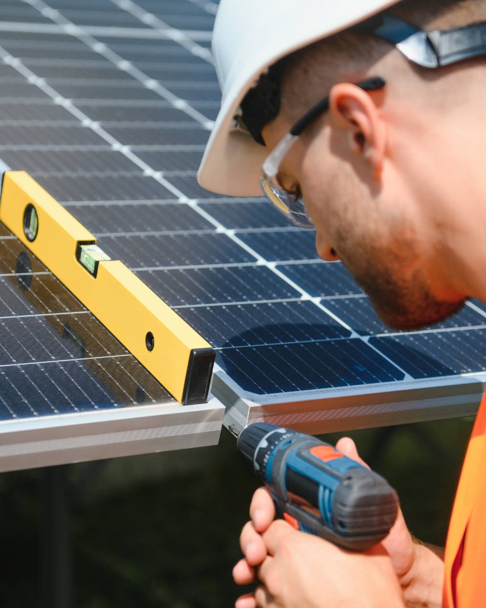 A contractor wearing a hard hat and safety glasses installs a solar panel.