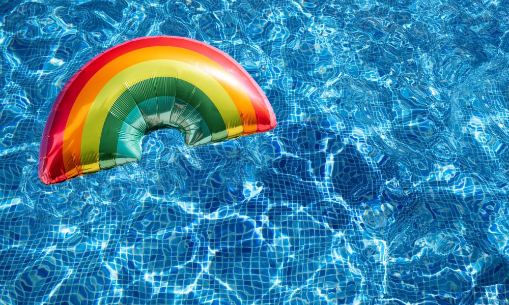 Clear blue pool water with a large rainbow shaped balloon floating
