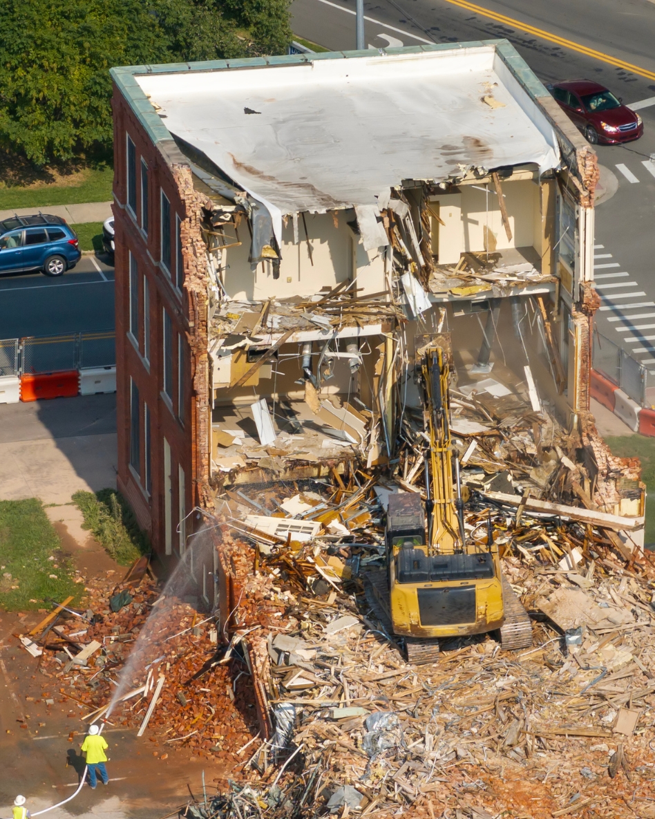 Heavy machinery demolishing a three story brick residential building.