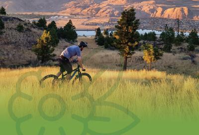 person riding a bike on a grassy trail with sagebrush hills in the background